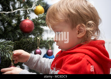 Felice adorabile bambina bambino in un abito rosso è preparare e decorare l'albero di Natale con splendidi giocattoli al tempo di vacanza Foto Stock