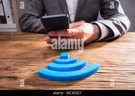 Close-up di commercianti la mano utilizzando il telefono cellulare con l'icona Wireless sulla scrivania in legno Foto Stock