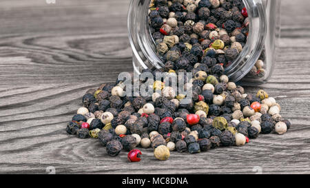 Mix di Peppe e contenitore per spezie. Piper nigrum. Chiudere decorative di  essiccato granelli di pepe spillato dal flacone di vetro giacente su un  sfondo di legno Foto stock - Alamy