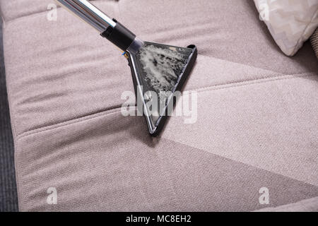 Angolo di Alta Vista di aspirapolvere sul divano sporco a casa Foto Stock