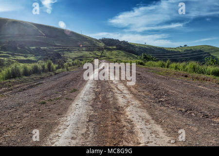 Strada di fango con tracce di pneumatici corre attraverso la valle verde in Malanje. Angola. L'Africa. Foto Stock