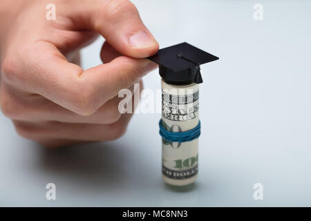 Close-up di mano di una persona immissione graduazione nera Hat su banconote americane Foto Stock