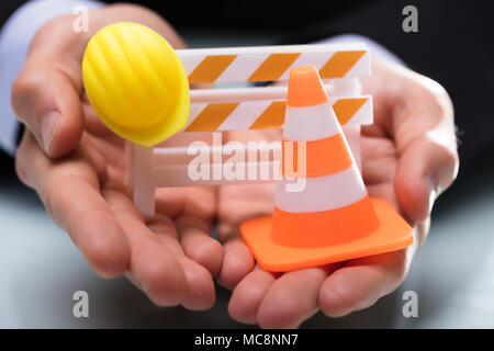 Close-up di persona della mano che tiene Barricade con cono di traffico e di elmetto Foto Stock