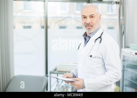 Coppia medico in camice bianco guardando la telecamera nelle sue cliniche durante la lettura del documento Foto Stock