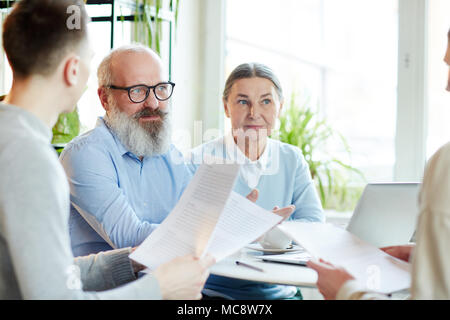 Due imprenditori senior in smart casual avente parlare con i loro colleghi più giovani alla riunione di lavoro Foto Stock
