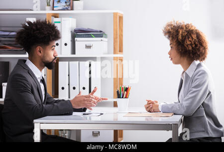 Vista laterale di due giovani imprenditori aventi la conversazione in ufficio Foto Stock