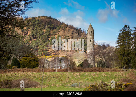 Stone torre rotonda e alcuni resti di un insediamento monastico originariamente costruito nel VI secolo nella valle di Glendalough, County Wicklow, Irlanda Foto Stock