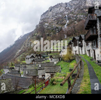 Tradizionale villaggio alpino con molte piccole case in legno e pietra e una cascata di montagna sullo sfondo Foto Stock