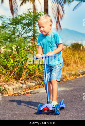 Carino boy riding kick scooter. Bambino di attività all'aperto Foto Stock