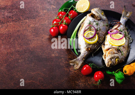 Cuocere al forno Grigliate di pesce, dorado, orata al limone, erbe e spezie e verdure su sfondo rustico. Vista dall'alto. Copia dello spazio. Foto Stock