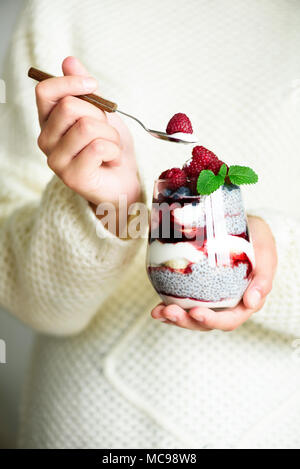 Ragazza in bianco maglione detiene il vetro con chia dessert di latte, Lamponi Mirtilli, menta. Colazione sana nozione. Spazio di copia, close up Foto Stock