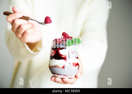 Ragazza in bianco maglione detiene il vetro con chia dessert di latte, Lamponi Mirtilli, menta. Colazione sana nozione. Spazio di copia, close up Foto Stock