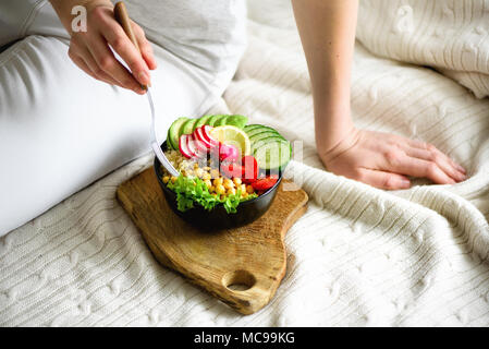 La ragazza tiene in mano, vegana detox buddha greggio ciotola con avocado, quinoa, cetriolo, Rafano, insalata, limone, pomodori ciliegini, ceci, chia semi sulla textil Foto Stock