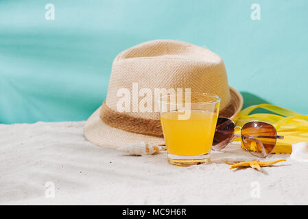 Estate sfondo. Beach Accessories flip flop, occhiali da sole e cappello e il succo di arancia su Sfondo sabbia Foto Stock