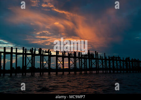 Amarapura, Myanmar - Novembre 2012: Al tramonto i monaci buddisti e persone attraversano U Bein Bridge, tornando a casa Foto Stock