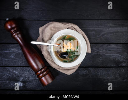 Zuppa di pesce, servito in tazza bianca con un cucchiaio, biancheria igienico e pepe macinino sullo sfondo di legno. Vista dall'alto. Foto Stock