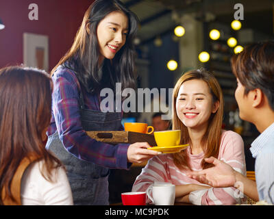 Giovani asiatici sorridente cameriera che serve caffè ai clienti. Foto Stock