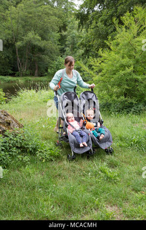 Mamma giovane che spinge un doppio buggy in vacanza con i gemelli. Foto Stock