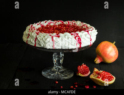 In casa torta di meringa Pavlova , fresco i semi di melograno e sugo sulla torta vintage stand su legno nero lo sfondo di texture. Foto Stock