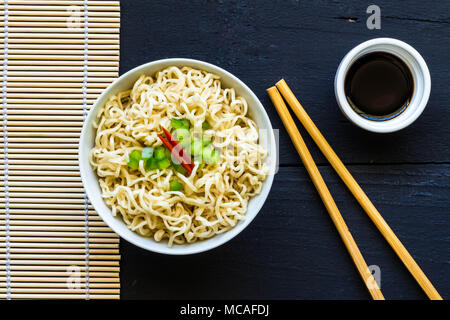 Recipiente di cottura istantanea plain tagliatelle con bacchette di bambù e il verde e pepe rosso guarnire - vista superiore foto Foto Stock