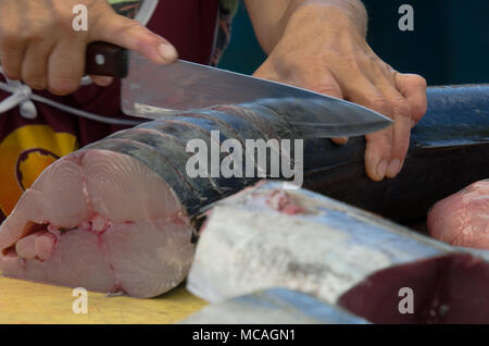 Close up mani femminili tenendo il coltello per affettare il pesce in preparazione per essere tagliato in filetti di salmone - outdoor mercato di frutti di mare Foto Stock