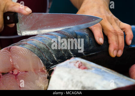 Close up mani femminili tenendo il coltello per affettare il pesce in preparazione per essere tagliato in filetti di salmone - outdoor mercato di frutti di mare Foto Stock