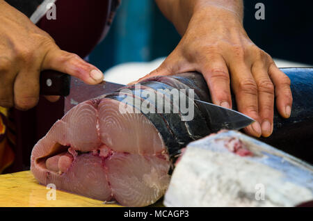 Close up mani femminili tenendo il coltello per affettare il pesce in preparazione per essere tagliato in filetti di salmone - outdoor mercato di frutti di mare Foto Stock