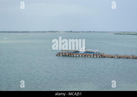 Blu e bianco barca il trasporto persone fermato nella vecchia marina, sfondo con isola tropicale e grigio blu cielo Foto Stock