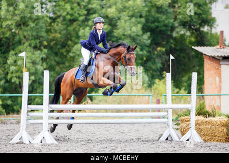 Ragazza giovane riding sorrel cavallo su show jumping concorrenza Foto Stock