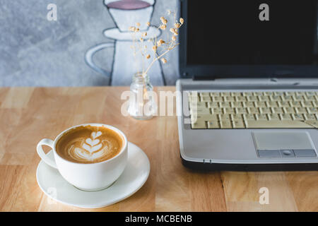 Una tazza di caldo cuore latte art caffè sul tavolo di legno, con il computer portatile. Foto Stock