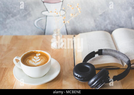 Una tazza di caffè latte, libro e le cuffie su un pavimento di legno. Il tempo per rilassarsi. Foto Stock