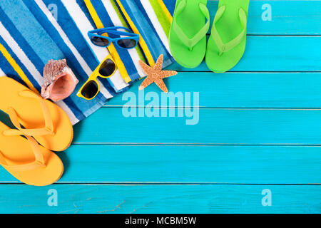 Scena di spiaggia con asciugamano a strisce, occhiali da sole, flip-flop, il Seashell e starfish prevista sul vecchio weathered legno blu di appontaggio. Spazio per la copia. Foto Stock