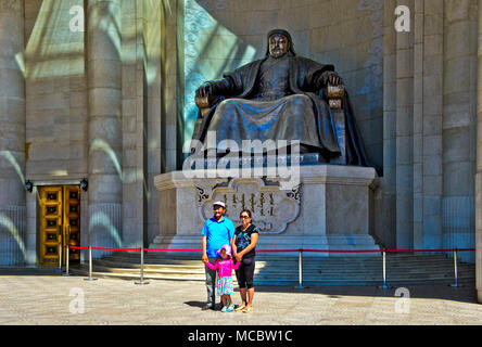 Il mongolo giovane con il bambino in piedi per una foto ricordo davanti alla Gengis Khan un monumento all'edificio del Parlamento sulla piazza Sukhbaatar, Ulaan Foto Stock