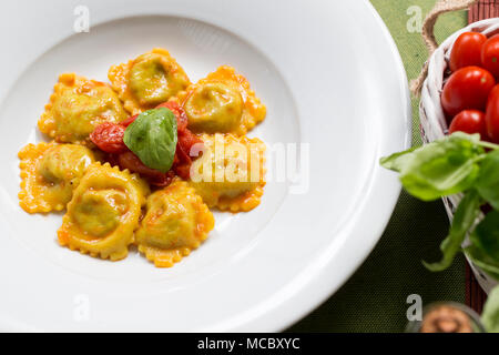 Una piastra di italian pasta ripiena, ravioli con salsa di pomodoro fresco, le foglie di basilico e olio di oliva con soggetti e concentrarsi sulla sinistra su un tavolo verde panno Foto Stock