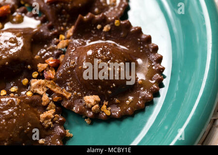 Primo piano di una piastra di italiano cioccolato vegano i tortelli di zucca, sul rop alcuni burro fuso e frantumato amaretto in una piastra verde Foto Stock