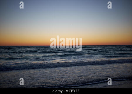 Colorato arancione tramonto al largo di Anna Maria Island, Florida su un oceano di calma con dolci onde che lambiscono la spiaggia Foto Stock