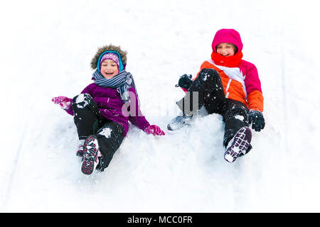 Due sorelle divertirsi insieme mentre lo scorrimento in discesa in inverno. Foto Stock