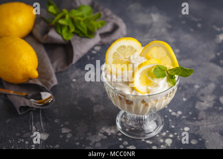 Limone dessert, limone inezia, cheesecake, panna montata, parfait. Mousse di frutta in vetro su uno sfondo scuro. Foto Stock