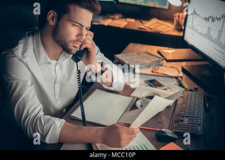 Commerciante di parlare al cliente sui tassi di cambio mentre si lavora fino a tardi in ufficio, analista finanziario avente la conversazione telefonica chiamando il cliente, stock br Foto Stock