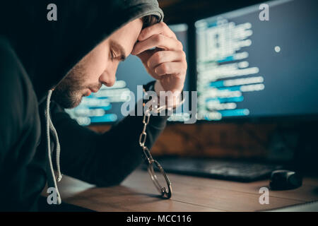 Arrestati sconvolto hacker o triste criminale di internet è stato preso per essere imprigionato seduta con la mano in manette sul computer codice sfondo, criminalità informatica legge Foto Stock