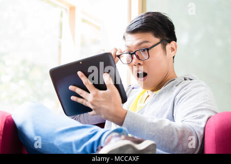 Giovane uomo asiatico sorpreso da online informazioni visualizzate su un tablet PC Foto Stock
