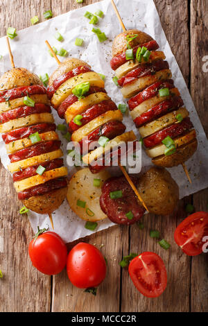 Semplice snack di spiedini di patate con salsiccia salame e cipolla verde vicino sul tavolo. Verticale in alto vista da sopra Foto Stock