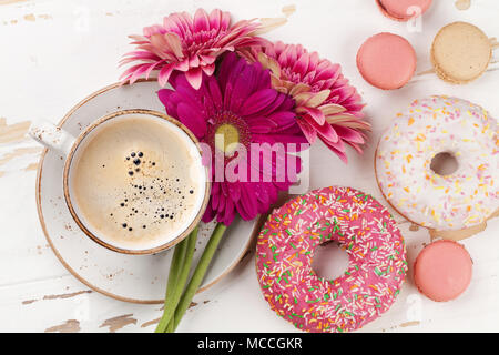 Tazza da caffè, ciambelle e gerbera fiori bianchi sul tavolo di legno. Vista superiore Foto Stock