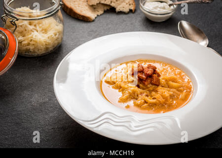 Cucina ceca zuppa di crauti con salsiccia e patate in bianco piatto blask sul tavolo di pietra Foto Stock