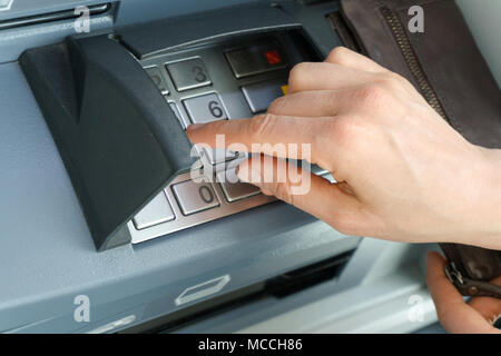 Mano femmina immettendo un codice PIN di sicurezza in corrispondenza di un punto di contanti o ATM da vicino e in dettaglio Foto Stock