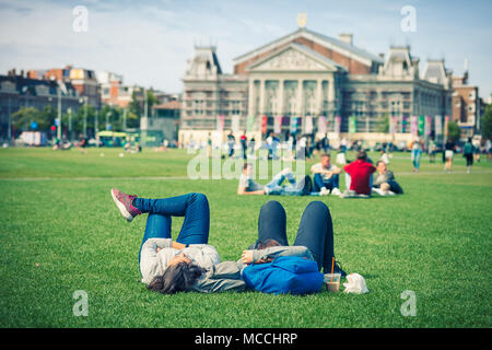Rilassata giovane su erba nel parco pubblico con il museo VanGogh sullo sfondo, Amsterdam, Olanda Foto Stock