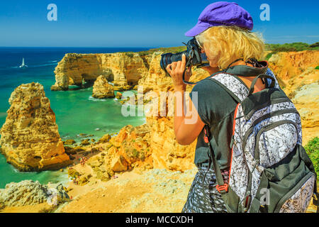 Viaggi fotografo prende shot iconica archi naturali di Praia da Marinha in Algarve. Turista femminile scatta foto con la fotocamera professionale di alte scogliere di popolari Marinha Beach. Viaggio in Portogallo Foto Stock