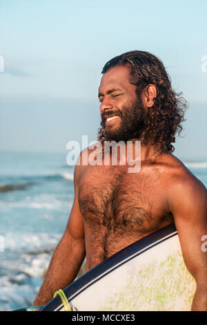 Il navigatore è in possesso di una tavola da surf su Indian Ocean Shore Foto Stock