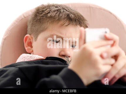 Completamente assorbito piccolo ragazzo giocando con il telefono cellulare giochi on line. Isolato su sfondo bianco. Foto Stock