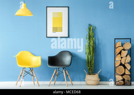 Sala di attesa interno in stile minimal contrastanti con il giallo e il nero Sedie, Lampada , Legna da ardere, pianta in un vaso e un poster su una parete blu Foto Stock